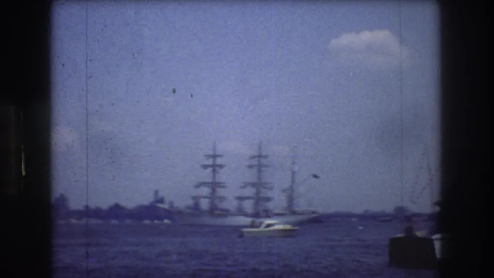 1976 New York City 8mm frame showing the sailing ship low on the horizon, a small motorboat in the foreground, blue water, bright sky, and soft film grain.