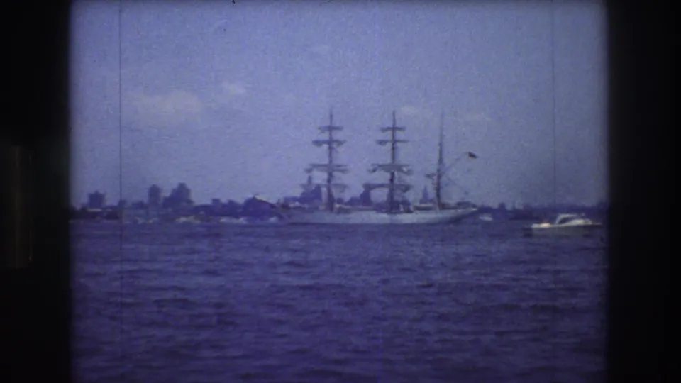 The sailing vessel remains centered on open water, framed by the soft focus and purple color cast of 1976 8mm footage near New York City.