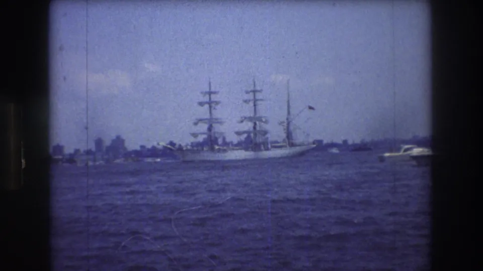 A final 1976 8mm frame shows the three-masted sailing vessel farther across the water, with a small boat nearby and New York City skyline forms softened by haze.