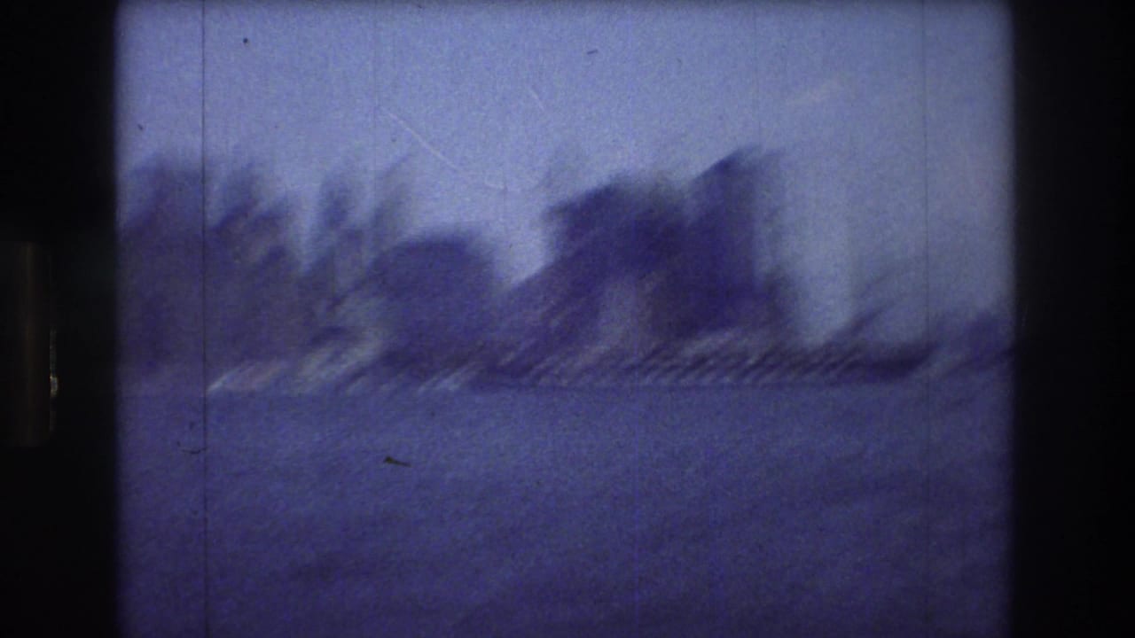 A soft, motion-blurred 8mm harbor view in New York City, with water in the foreground and a dark shoreline or tree-covered landform in the distance.