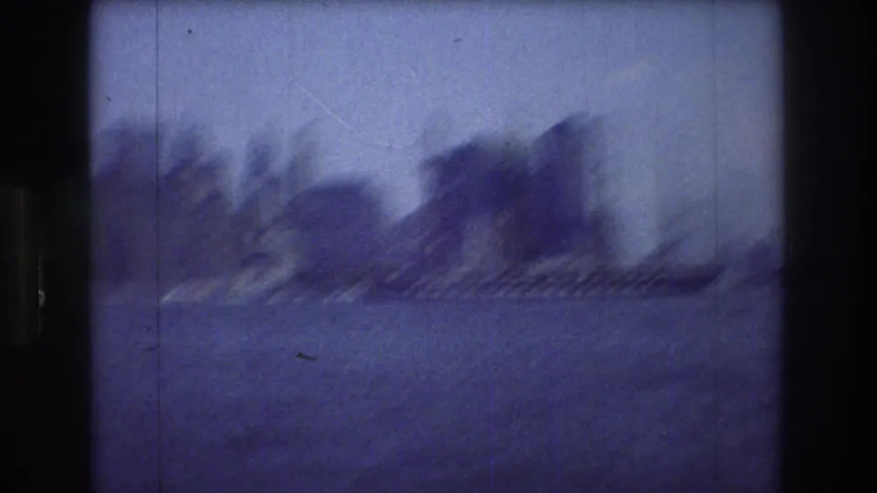 A soft, motion-blurred 8mm harbor view in New York City, with water in the foreground and a dark shoreline or tree-covered landform in the distance.