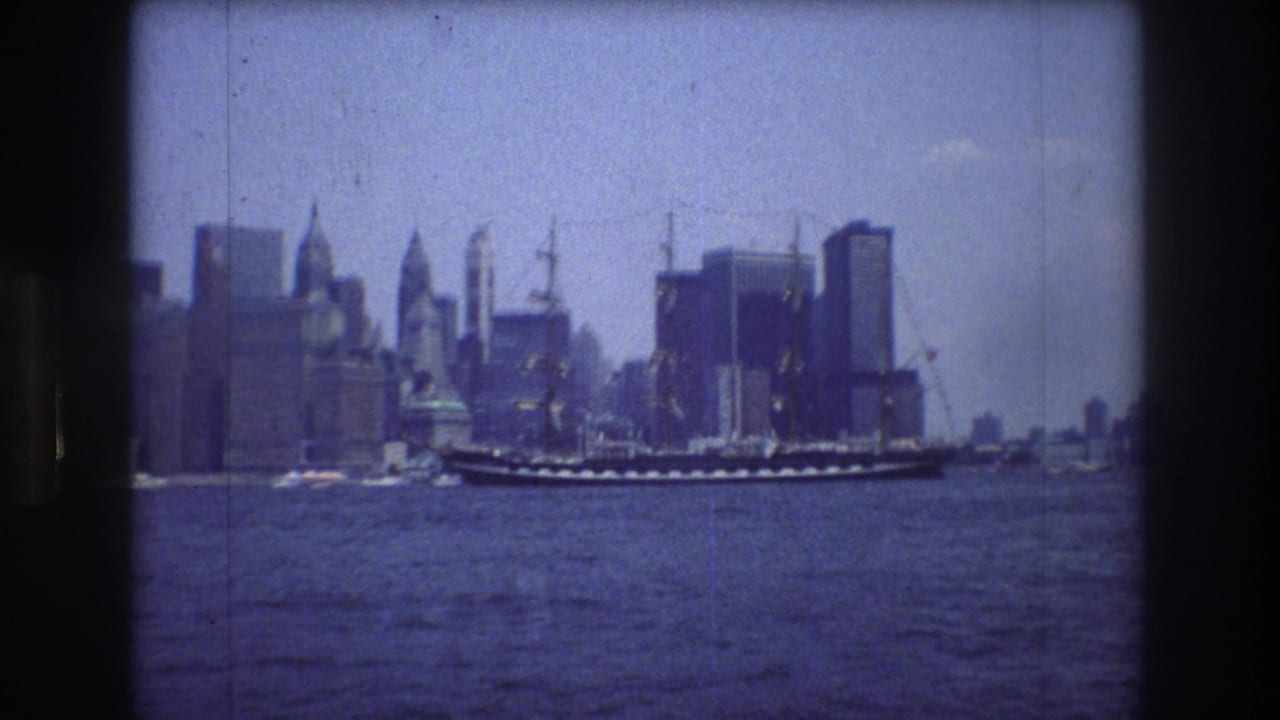 The ship appears near the center of the frame, its masts and rigging silhouetted against the Manhattan skyscrapers and pale blue sky.
