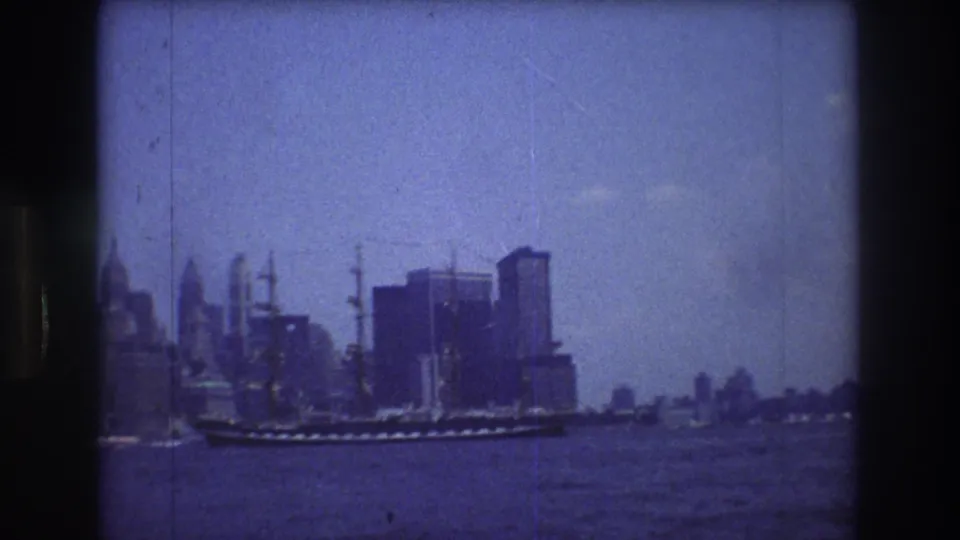 The vessel continues across the harbor in front of the New York City skyline, with soft 8mm focus and blue-tinted color visible in the frame.