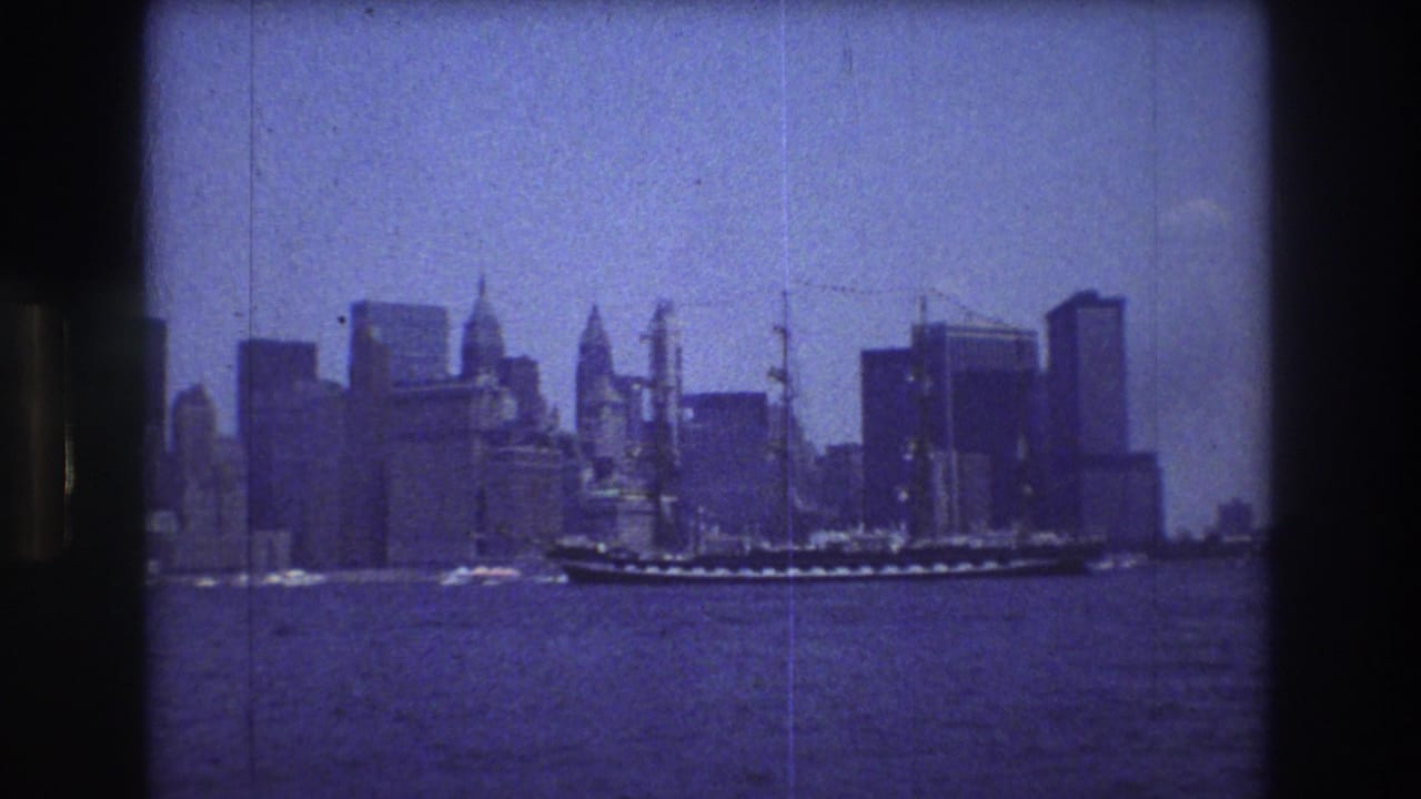 Tall-masted ship crossing river water in front of a hazy city skyline.
