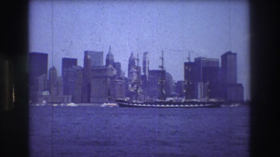 The tall ship appears mid-frame on the river, with New York City high-rises and waterfront buildings visible behind it in blue-tinted 8mm footage.