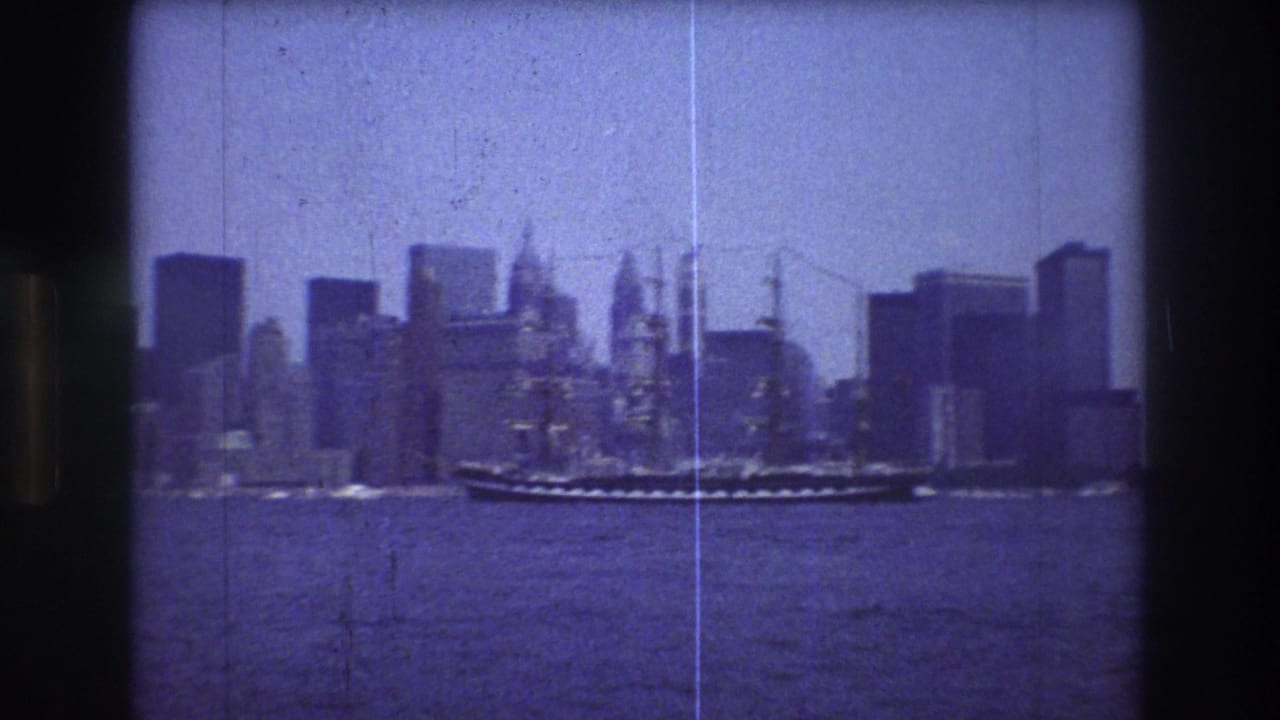 Sailing ship centered on harbor water with skyscrapers across the background.