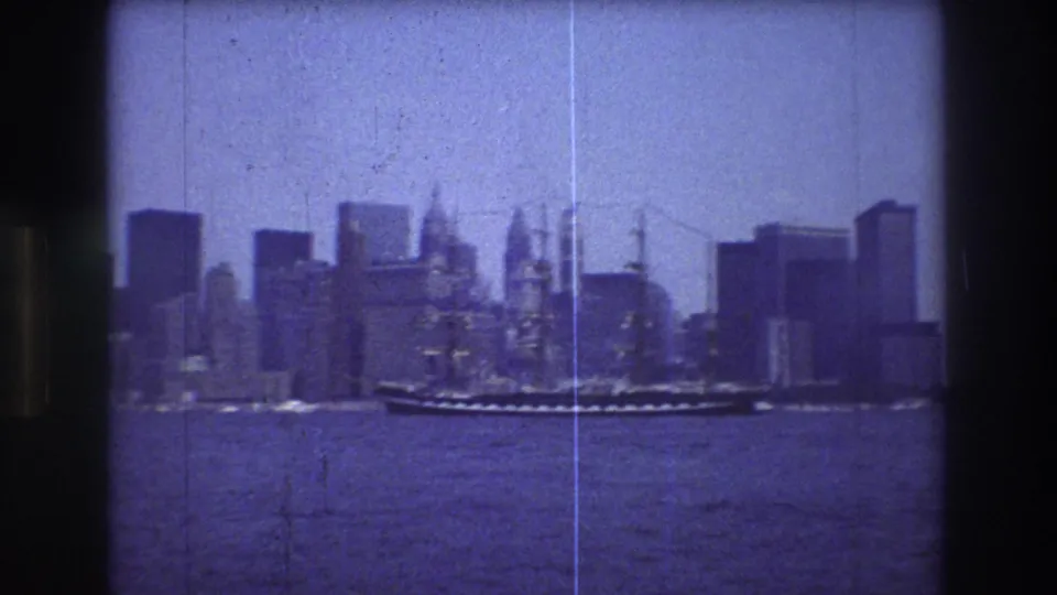 The sailing ship appears more centered against the New York City skyline, with choppy harbor water, high-rise buildings, soft focus, and visible 8mm film scratches.