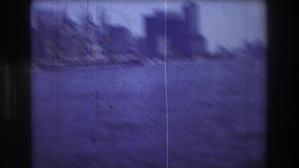 The final frame shows motion-blurred harbor water and a dark urban skyline during the pan, with the ship faintly at the left and heavy grain, scratches, and blue-purple color shift.