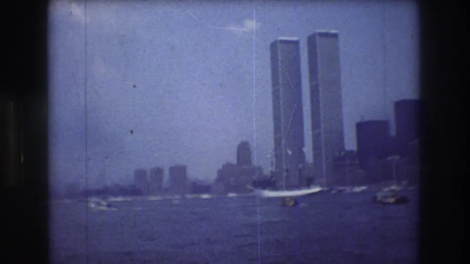 1976 New York City skyline seen across the water, with the Twin Towers prominent and small boats moving in the foreground.