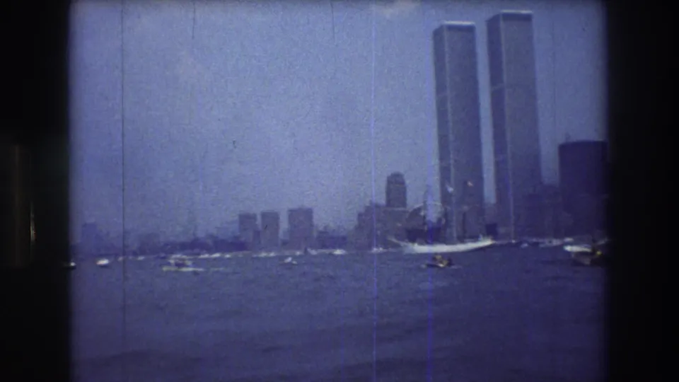 Wide 1976 New York City harbor view with the World Trade Center towers on the skyline and several boats crossing the water.