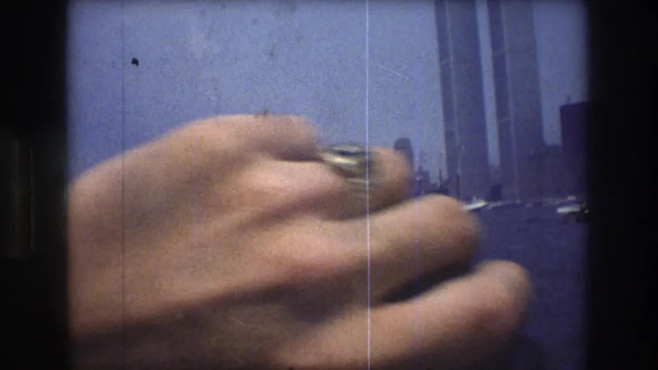 A foreground hand partially obscures a 1976 New York City waterfront view, with the Twin Towers and harbor still visible beyond it.