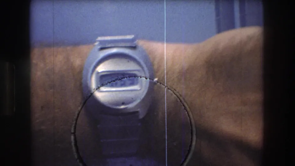A wristwatch fills the foreground while the 1976 New York City harbor skyline, including the Twin Towers, remains blurred behind it.