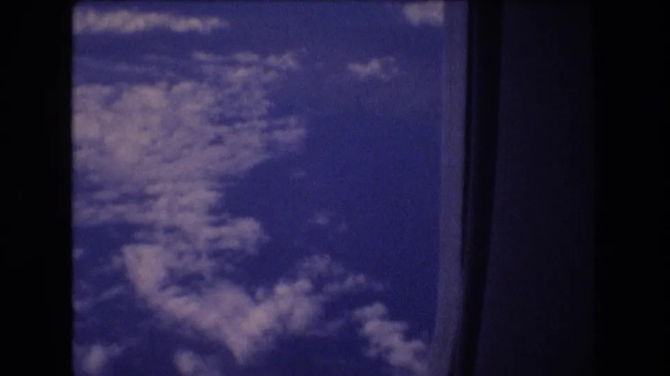 Aerial cloudscape from an airplane passenger window, with blue 8mm color shift, soft cloud detail, and dark vertical framing from the aircraft window or scan edge.