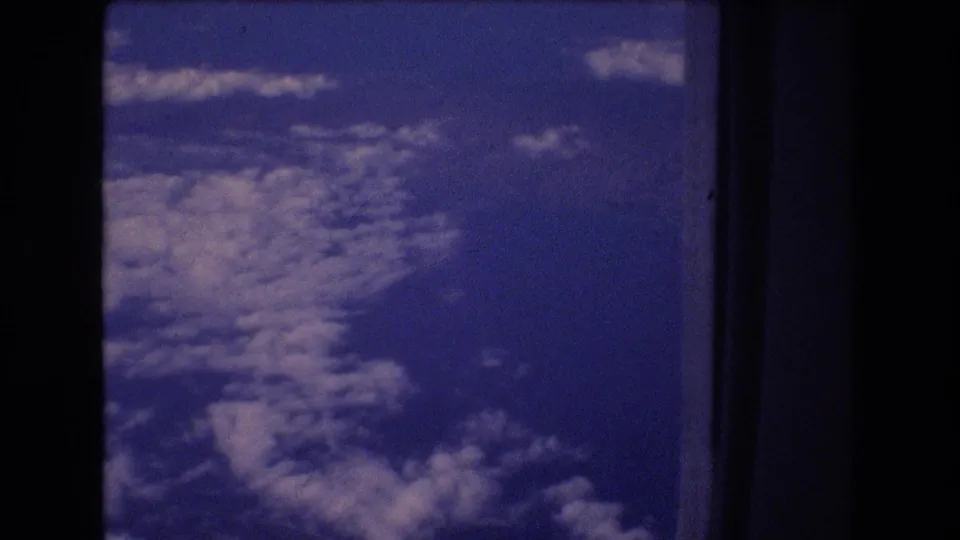 Vintage 8mm frame of layered white clouds below a blue sky, recorded from a passenger viewpoint during travel associated by metadata with Honolulu, Hawaii in 1977.