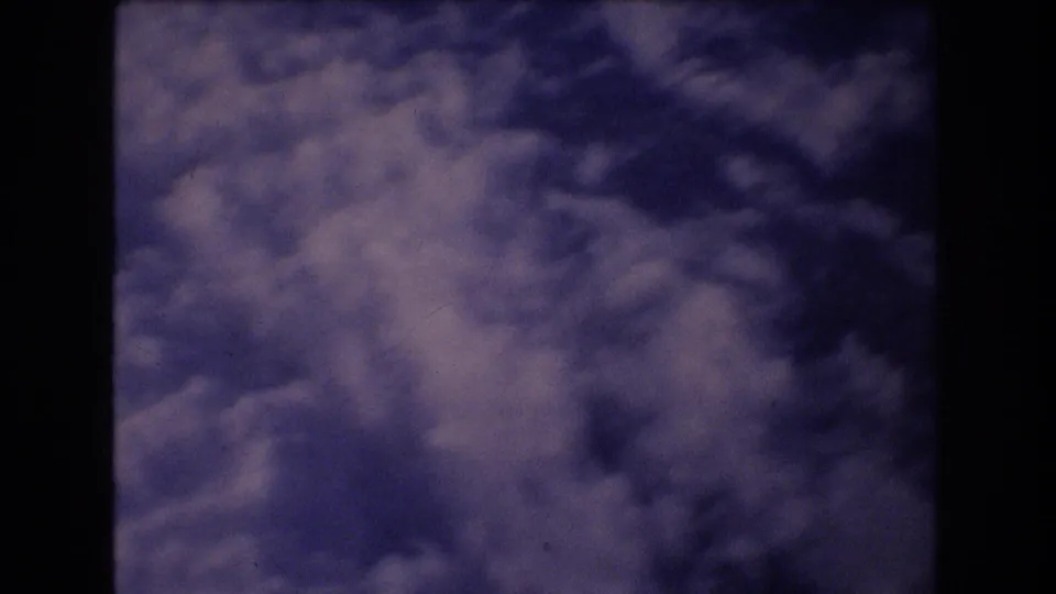 The final frame shows a hazy cloud field and blue sky through the dark framing of an airplane window, with visible 8mm grain and color shift.