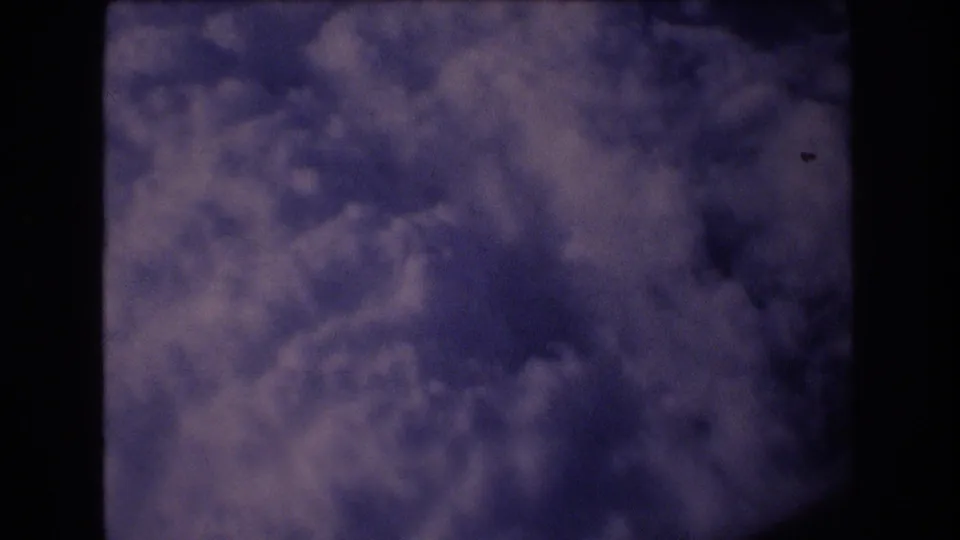 1977 8mm passenger-window view toward dense blue-purple clouds, with the dark aircraft window edge framing the scene.