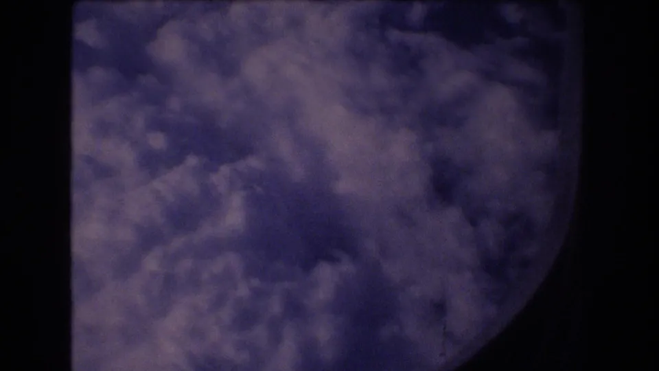 A passenger-window view from the 1977 Honolulu travel footage shows layered clouds beyond a dark rounded aircraft window edge.