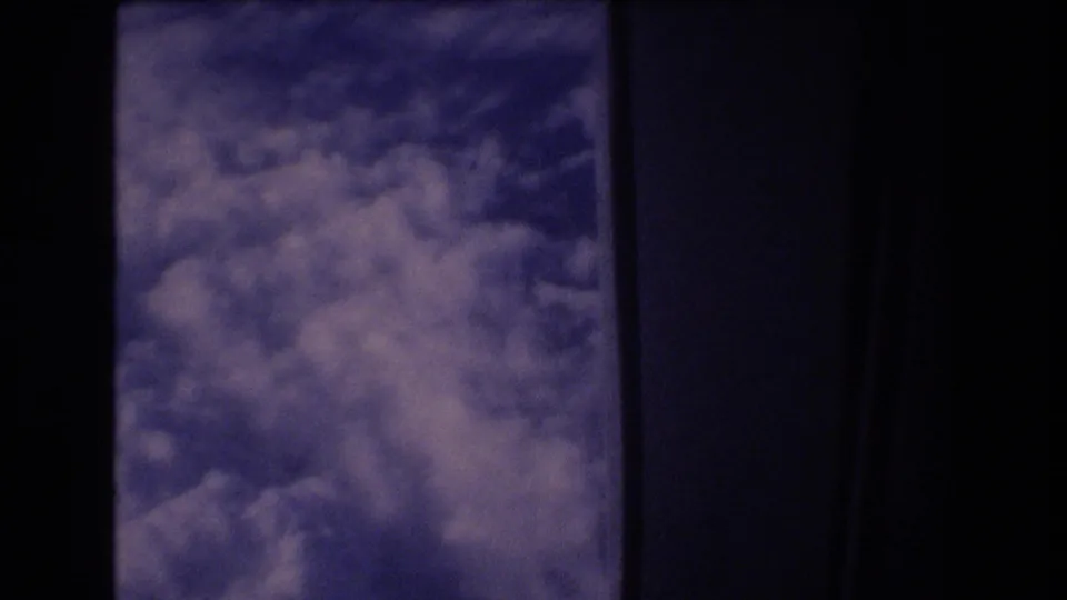 The lower portion of the passenger-window view shows textured cloud cover, dark interior window framing, and 8mm grain.