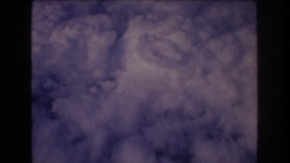 A final 1977 8mm frame holds on soft cloud forms outside the aircraft window, with dark interior edges and visible film texture.