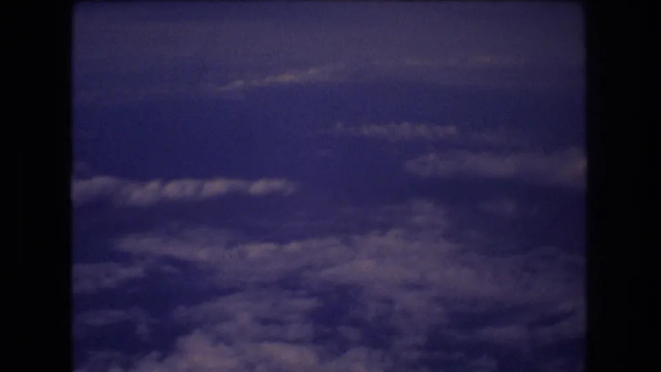 In-flight 8mm view with a band of darker blue sky above lower cloud layers, framed by the dark interior edges of the airplane window.
