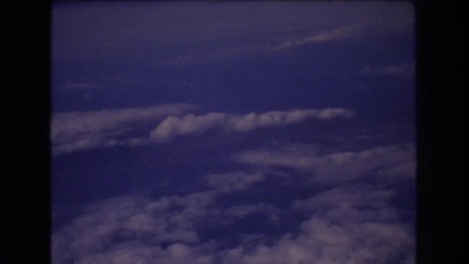 The final frame shows scattered cloud bands beneath a dark airplane-window edge, maintaining the quiet passenger-view perspective of the archival 8mm travel footage.
