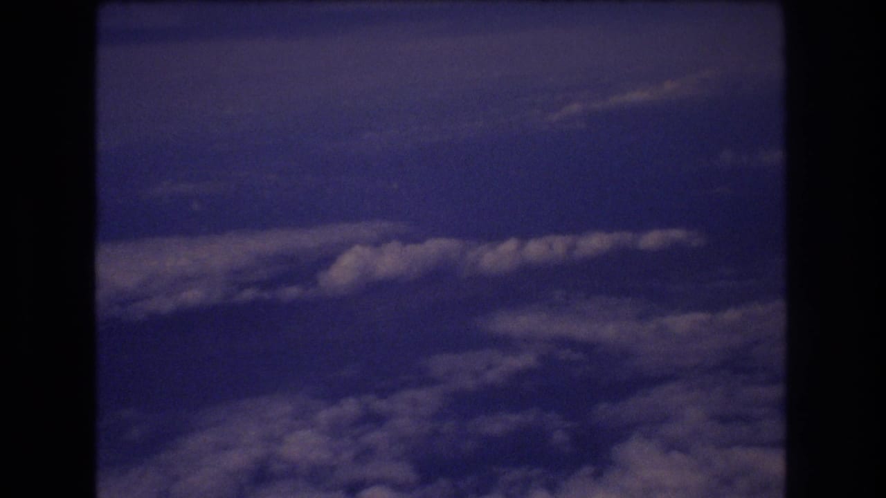 1977 8mm home-movie view of blue sky and layered clouds from inside an airplane window during travel associated with Honolulu metadata.