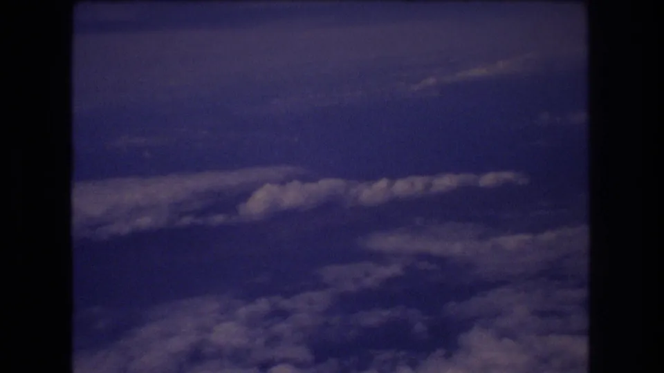1977 8mm home-movie view of blue sky and layered clouds from inside an airplane window during travel associated with Honolulu metadata.