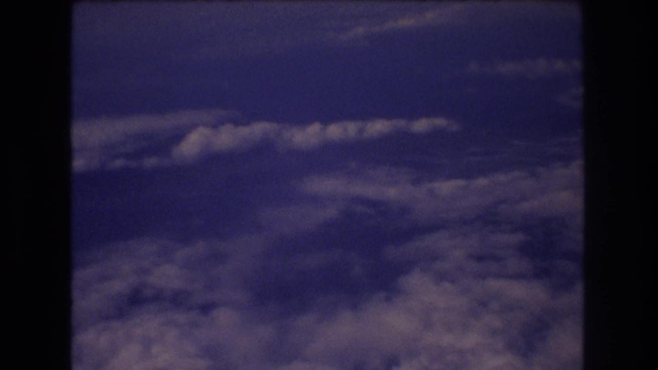 Aerial cloudscape framed by the dark edges of an airplane window.
