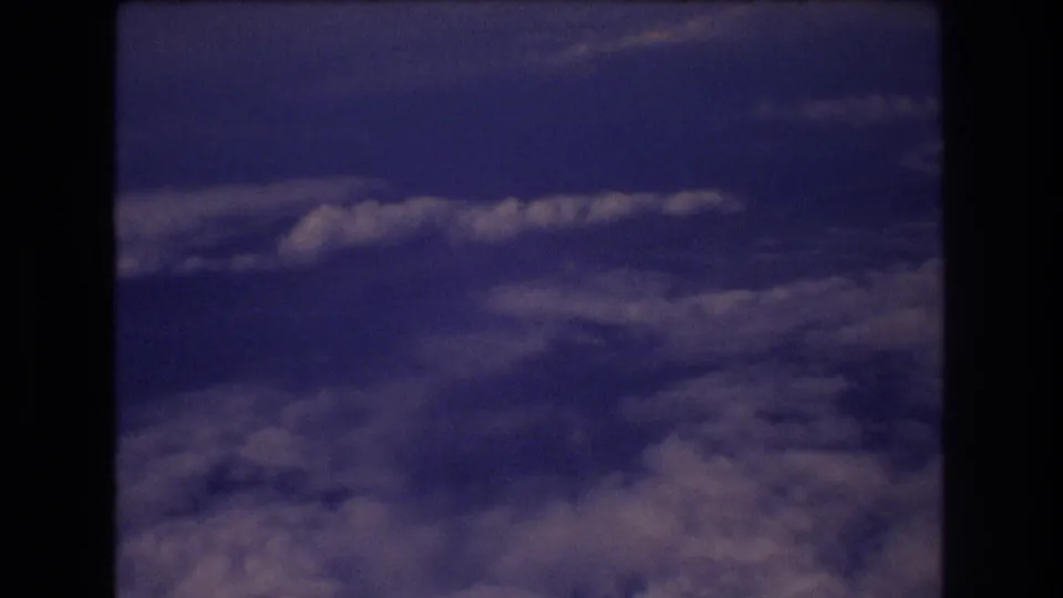 A steady 8mm airplane-window view shows blue sky, scattered cloud bands, and a broad cloud layer below, with Honolulu travel context supplied by clip metadata.