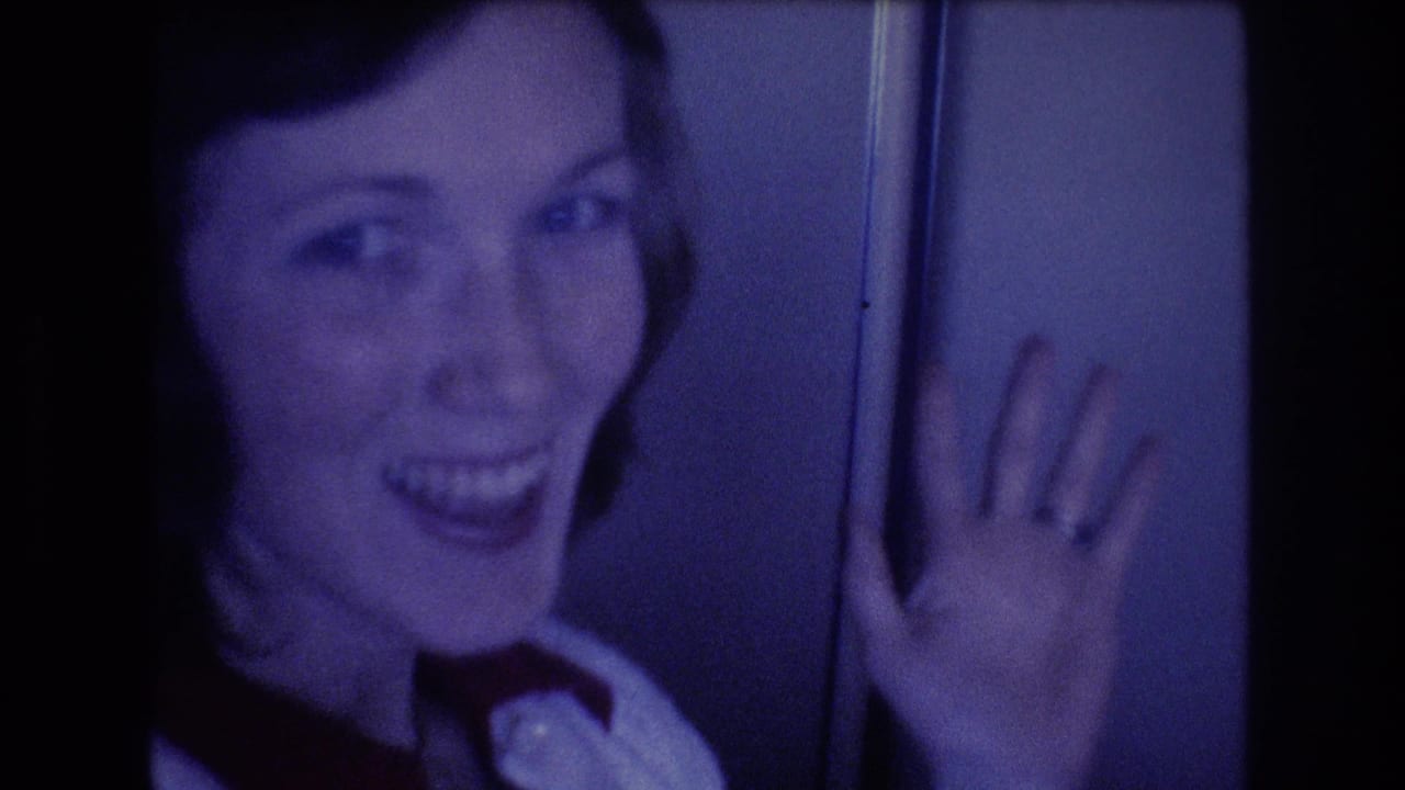 A young woman in a white collared shirt and dark tie smiles and raises her hand toward the camera during a 1977 home-movie airplane shot associated with Honolulu travel metadata.