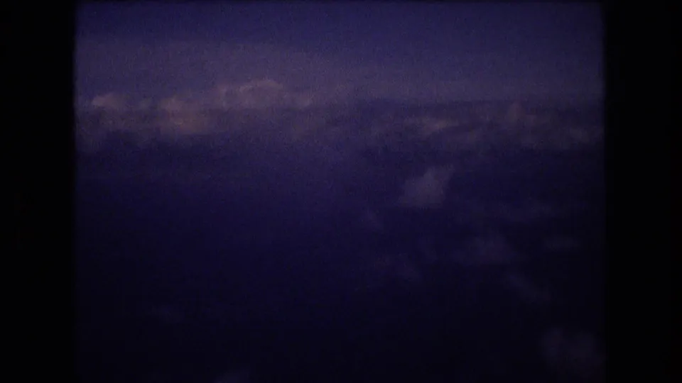 Blue-purple 8mm footage shows cloud layers and distant sky from above, likely filmed through an airplane window during the travel sequence.
