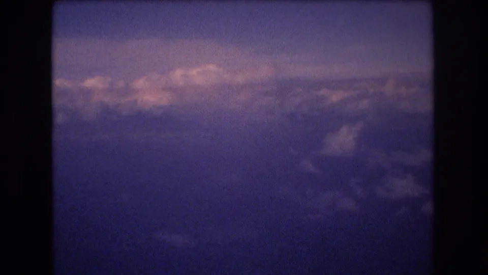 A wide 8mm airplane-window view shows clouds and sky with dark vertical frame borders and a pronounced blue-purple cast.