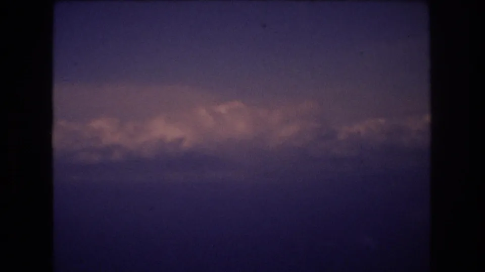 1977 8mm airplane-window view with a low band of pink-lit clouds beneath a darker blue-purple sky, framed by the contact sheet's black borders.