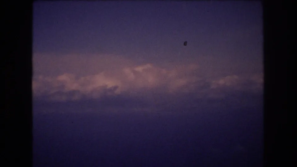 A final 1977 8mm frame shows dusk clouds tinted pink below a purple-blue sky, with dark home-movie frame borders and small visible film specks.