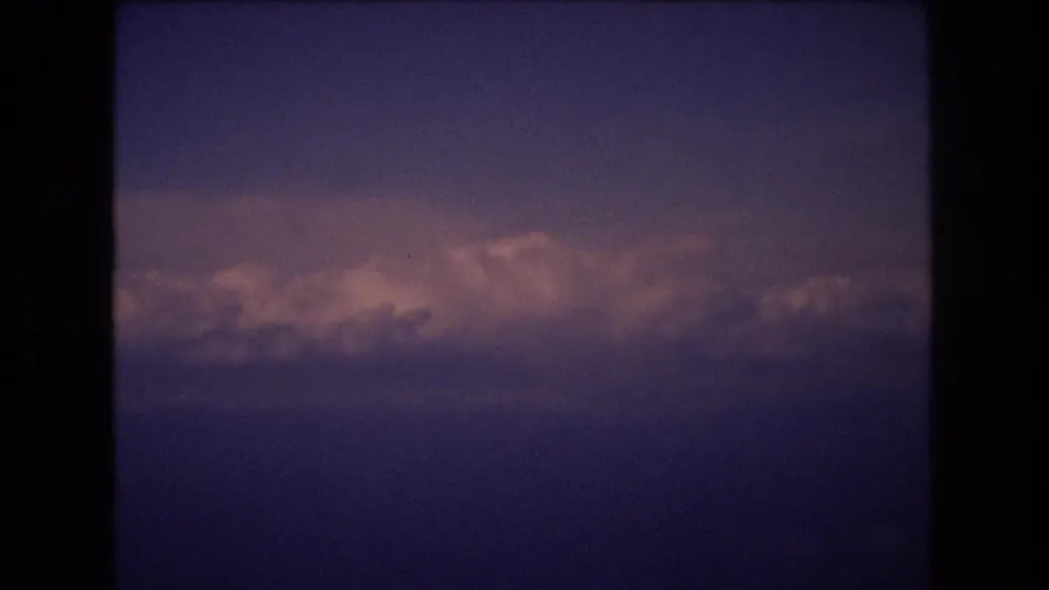1977 8mm home-movie frame associated with Honolulu travel footage, showing layered clouds lit by pinkish light against a purple-blue sky with dark rounded borders.