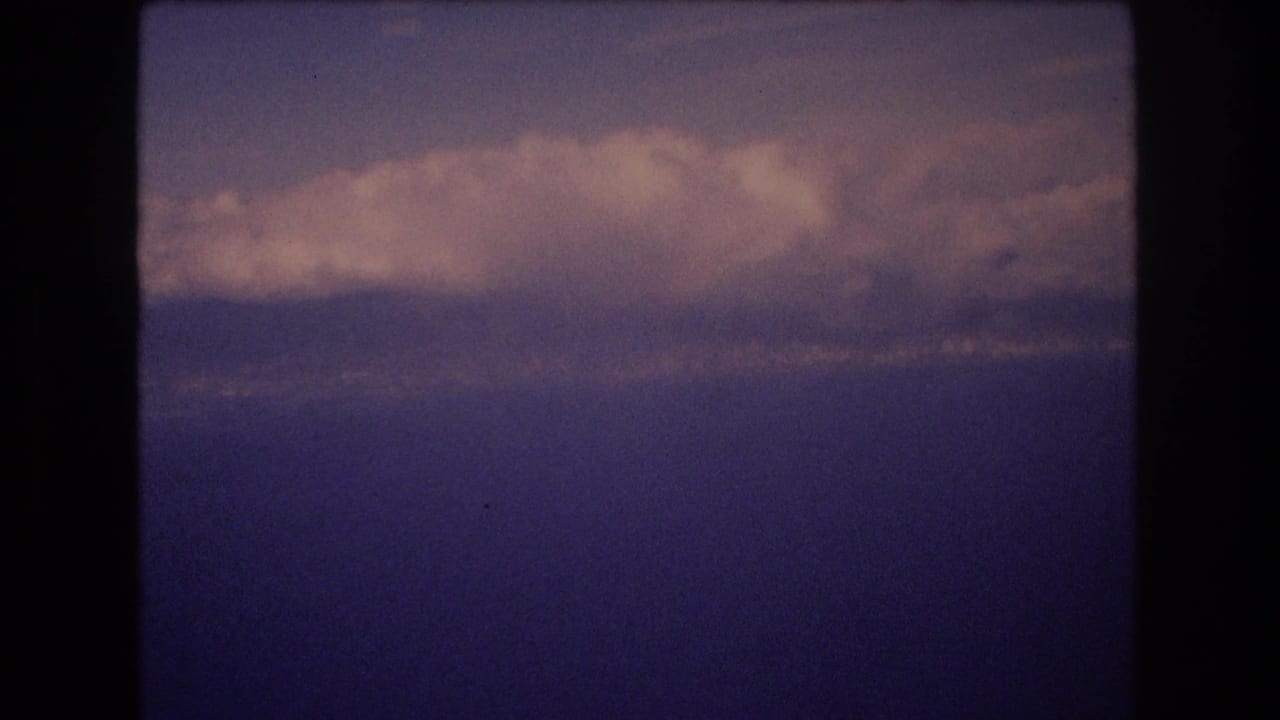 Blue water and layered clouds viewed through a dark plane-window edge.