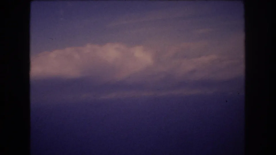 Vintage 8mm aerial view with a soft cloud bank crossing the lower part of the frame and blue water or haze beyond.