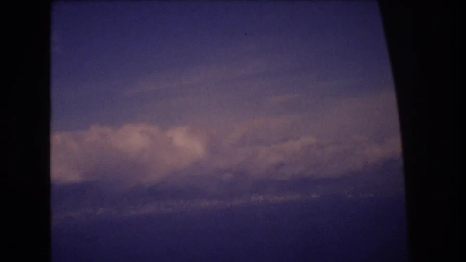 Final frame of the 1977 Honolulu-labeled home-movie clip showing clouds over a blue water horizon through dark in-flight window framing.