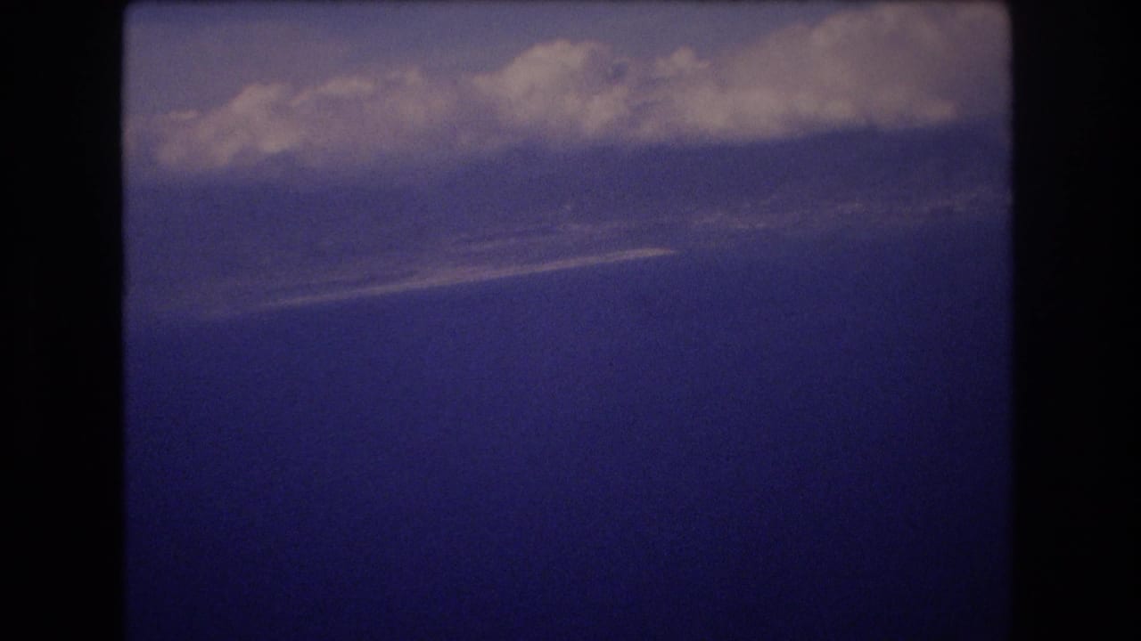 1977 Honolulu home-movie frame showing a dark blue sky with thick pale clouds near the upper edge and visible film grain.