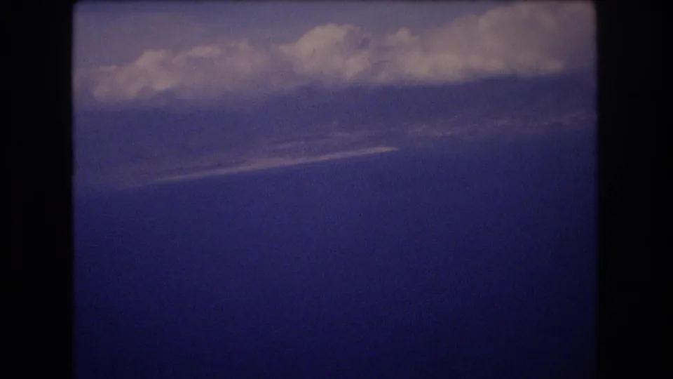 1977 Honolulu home-movie frame showing a dark blue sky with thick pale clouds near the upper edge and visible film grain.