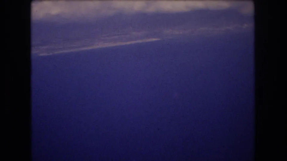 1977 Honolulu home-movie frame showing a broad field of dark blue sky beneath a pale, slightly blurred cloud layer.