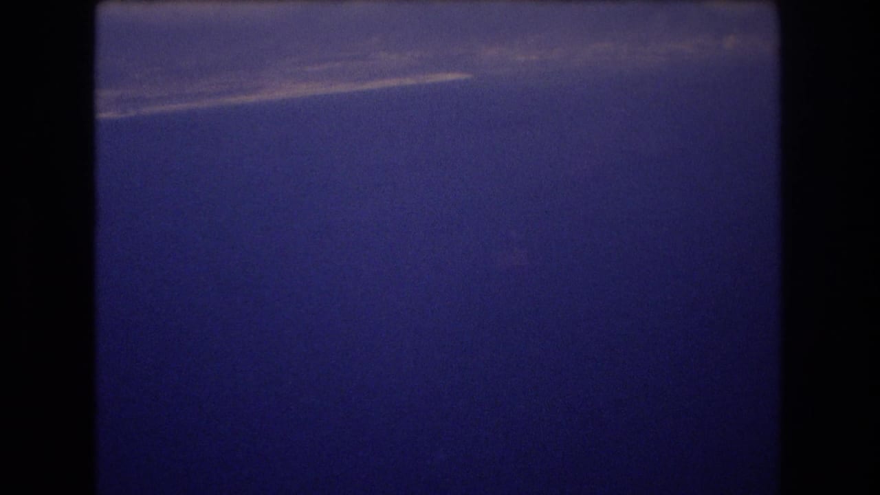 1977 Honolulu 8mm frame showing a saturated blue sky with a faint light streak near the top and visible film grain along the gate edges.