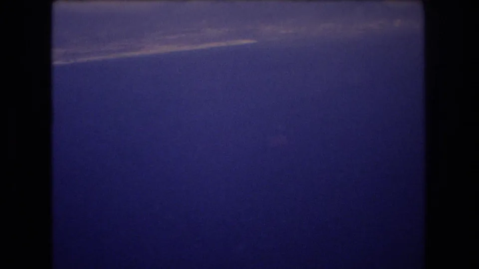 1977 Honolulu 8mm frame showing a saturated blue sky with a faint light streak near the top and visible film grain along the gate edges.
