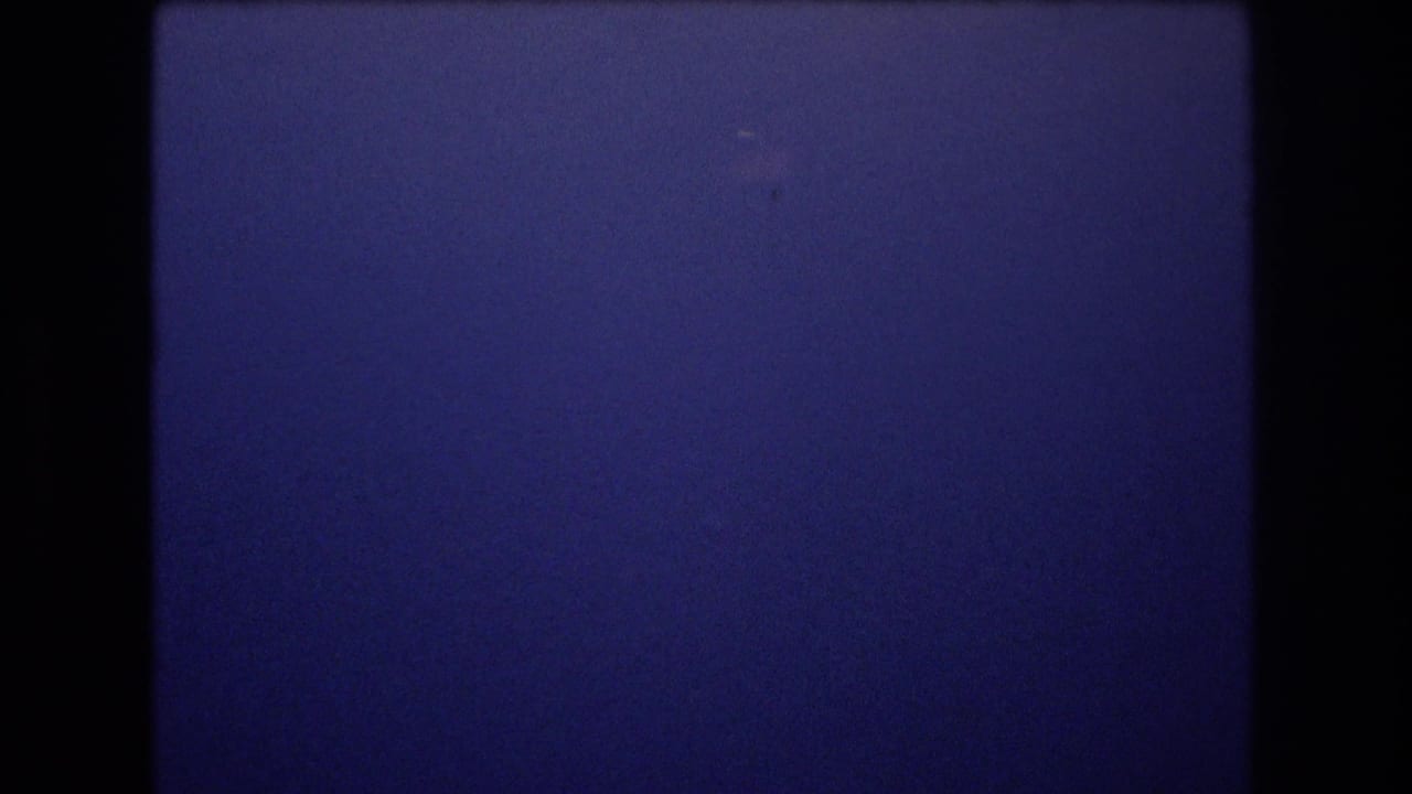 Mostly clear blue sky with dark frame edges and small specks in the film image.