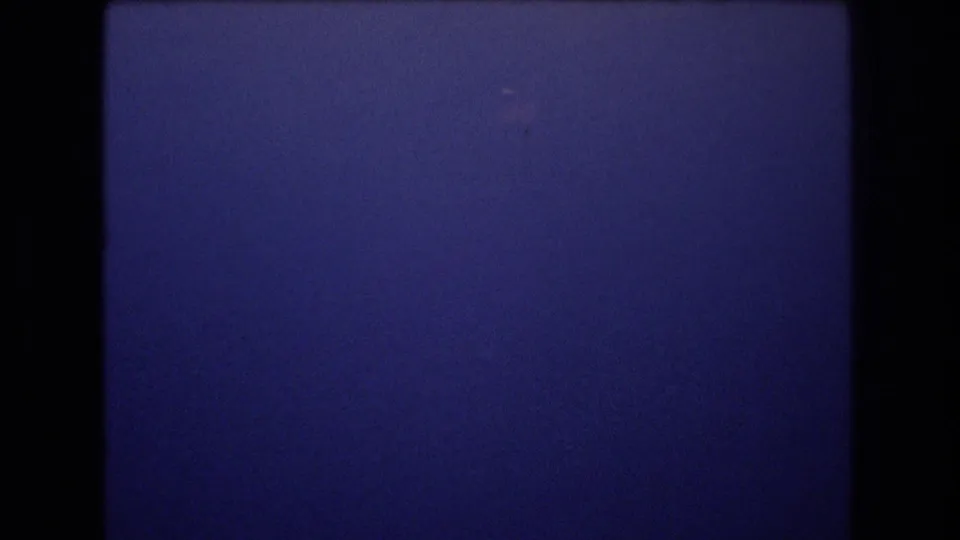 1977 Honolulu 8mm frame of a largely clear blue sky, bordered by the film gate and marked by fine grain and tiny specks.