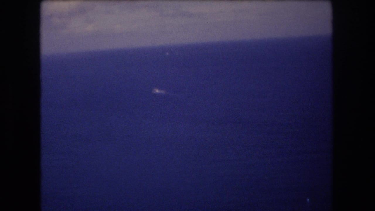 1977 Honolulu-area 8mm frame showing a small white boat far out on a calm blue ocean below a soft, level horizon.