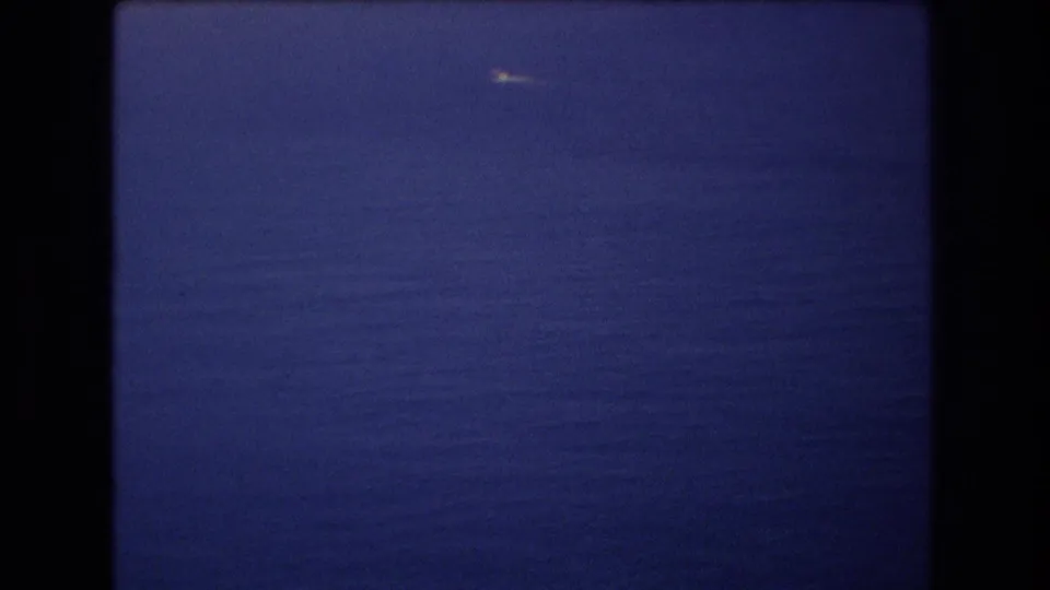 1977 Honolulu-area 8mm frame with open blue water, a soft horizon, and a small bright boat moving across the distant sea.