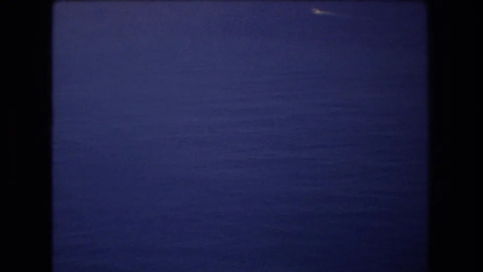 1977 Honolulu-area 8mm frame showing a tiny white boat near the horizon over a calm expanse of blue ocean.