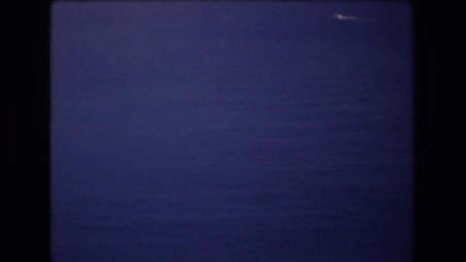 1977 Honolulu-area 8mm frame holding on a small bright boat against a wide calm ocean with a muted blue horizon.