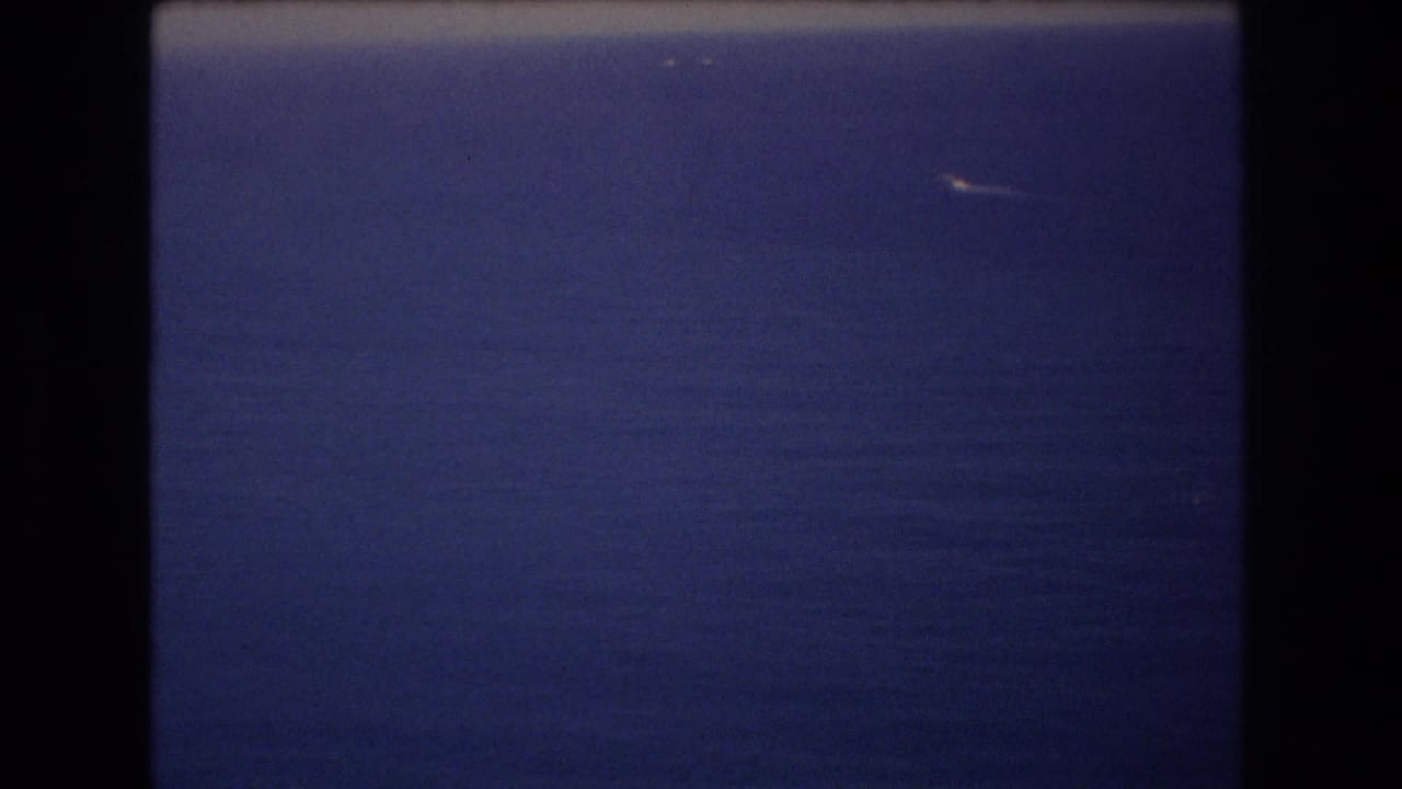 1977 8mm frame from near Honolulu showing deep blue ocean, a pale horizon band, and a small white distant object or wake against the water.